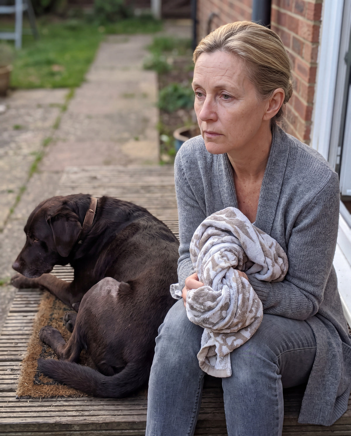 Woman sitting on a back step with a twisted towel, her large dog lying beside her